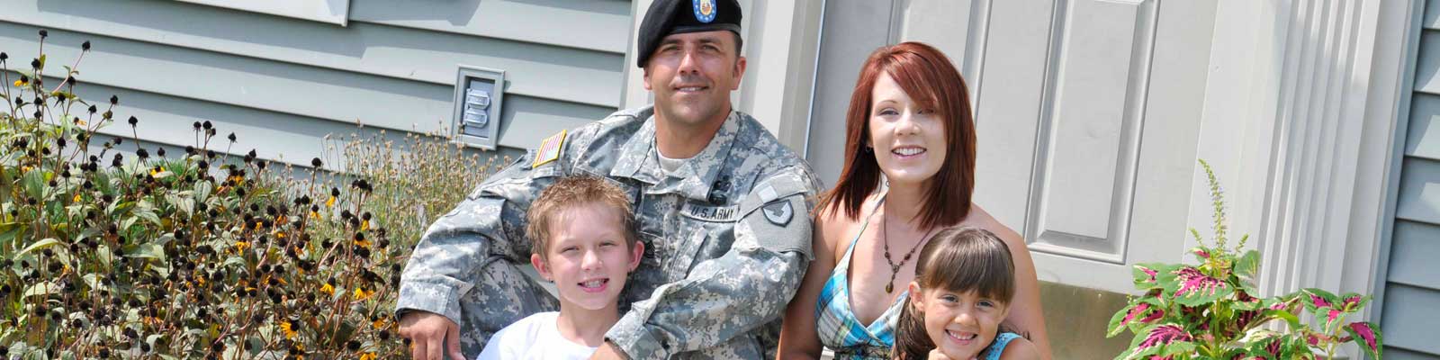 Smiling military family of 4 in front of house