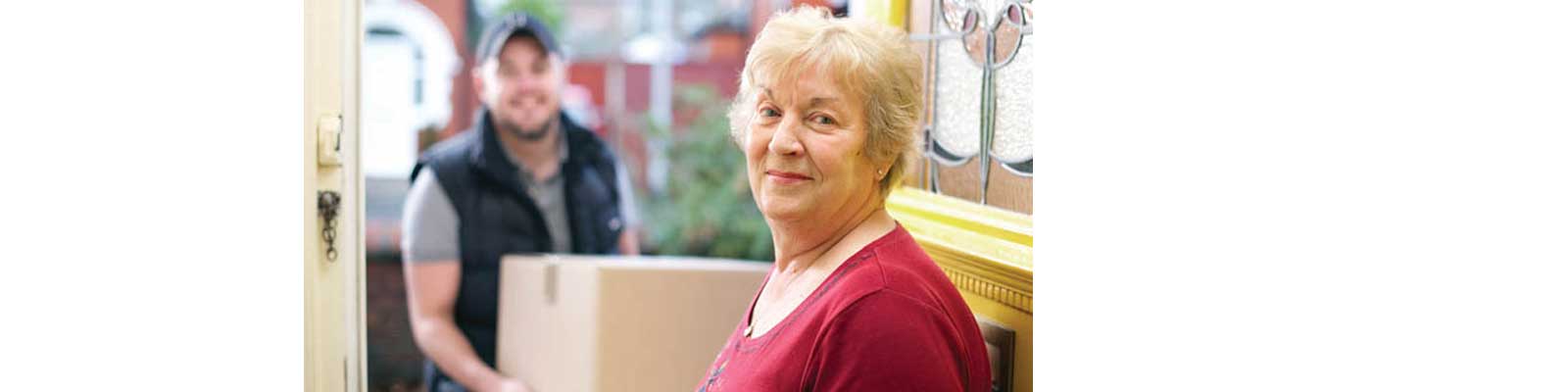 Mover with box at the front door of happy female senior